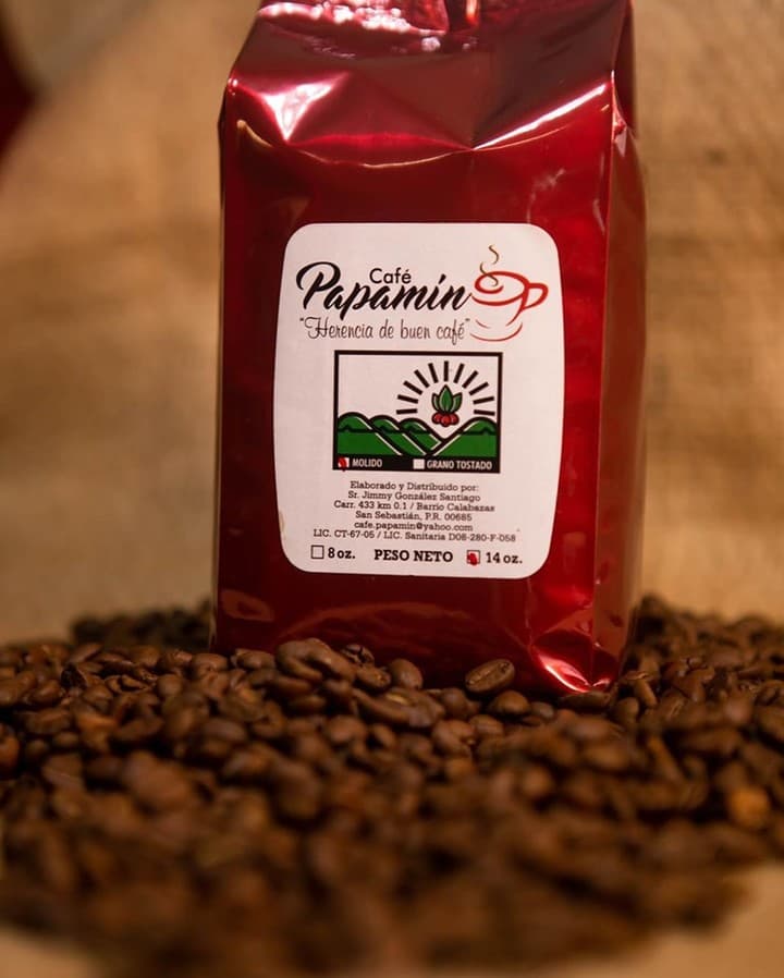 Café Papamín - Presentación profesional del producto premium Una bolsa de Café Papamín, con su distintivo empaque rojo y etiqueta 'Herencia de buen café', rodeada de granos de café tostados, lista para ser disfrutada.